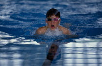 Boy wearing swimming goggles doing breaststroke in indoor pool.
