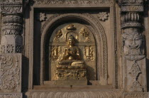 Buddha image carved in golden section of niche in wall.