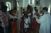 Church interior with priest conducting christening service  three women standing holding babies with other guests and family members.3 Asia Asian Bharat Female Woman Girl Lady Inde Indian Intiya Kids...
