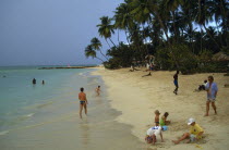 People and children playing on shore of sandy beach fringed by palm trees.Beaches Caribbean Kids Resort Seaside Tobagan Tourism West Indies