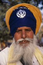 Portrait of a sikh man wearing orange and royal blue  turban set with a khanda  the symbol of Sikhdom and with grey beard and moustache.Asia Asian Bharat Gray Inde Indian Intiya Male Men Guy Old Seni...