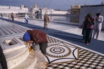 Barefooted pilgrims saying prayers at Golden Temple complex with offering of marigold flower garland lying on marble step.Asia Asian Bharat Inde Indian Intiya Religion Religious