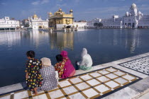 Golden Temple.  Sikh women and children sitting at the side of the sacred pool looking towards the temple.Asia Asian Bharat Female Woman Girl Lady Inde Indian Intiya Kids Religion Religion Religious...
