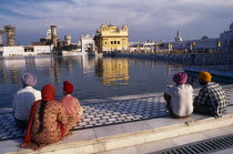 Sikh men  woman and child sitting on marble walkway beside the sacred pool looking towards the Golden Temple reflected in the water.Asia Asian Bharat Children Female Women Girl Lady Inde Indian Intiy...