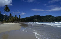 Sandy beach with couple lying in the surf and tree covered headland beyond.Beaches Caribbean Resort Seaside Shore Tourism Trini Trinidadian West Indies