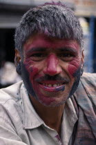 Head and shoulders portrait of man with face covered in pink and black coloured powderdye during Holi Festival.