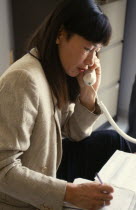 Woman using landline telephone and making notes on paper beside her.