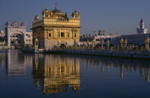 Golden Temple with pilgrims and visitors on causeway or the Guru s Bridge leading to temple reflected in rippled surface of pool.Asia Asian Bharat Inde Indian Intiya Religion Religious