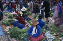 Vegetable stalls on the ground in cobbled a market place. Crowds of people.