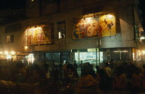Rickshaw wallahs in front of cinema with posters advertising films above the entrance  illuminated at night.Asia Asian Bangladeshi Nite