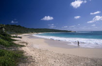 View over sandy beach and semicircular bay with woman walking along the waters edge.Beaches Caribbean Female Women Girl Lady One individual Solo Lone Solitary Resort Seaside Shore Tourism West Indies