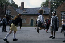 Primary schoolchildren playing skipping games in playground.