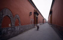 The Forbidden City.  Cyclist on narrow street between red painted walls.
