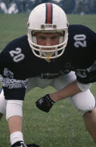 British American footballer wearing body protector and helmet in defensive stance.