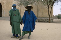 Two Touareg men in traditional dress holding hands.