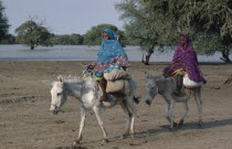 Baggara Arabs.  Two women from the Beni Halba tribe riding donkeys past lake.