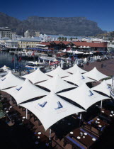 Victoria and Alfred Waterfront with view across white  awnings towards waterside restaurant and bars with boats docked in marina. Table Mountain behindAfrican Scenic