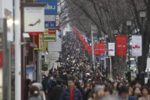 Shoppers crowd on the busy Omotesando-dori street  a row of trees along the road and banners on the lampposts.Asia Asian Japanese Nihon Nippon