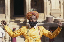 Portrait of man displaying the World s Longest Moustache and wearing beard net and gold coloured jacket.  Colored