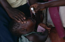 Health worker administering immunization polio drops to child in area near Gulu.  Partly funded by Comic Relief.