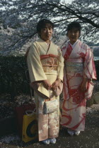 Two young women wearing traditional kimonos whilst stood under a cherry blossom tree.Asia Asian Japanese Nihon Nippon Female Woman Girl Lady