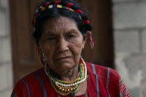 Head and shoulders portrait of elderly Cakchiquel Maya woman wearing traditional dress  hair braids and jewellery.
