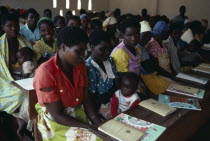 Adult literacy class for refugees from Mozambique in Kunyinda Camp.  Classroom of young women  some with children sitting at long wooden desks.reading  writing African Eastern Africa Female Woman Gir...