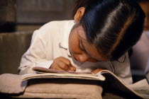 Little girl  head bent forward in concentration over exercise books in primary school class.reading  writing Asia Asian Kids Learning Lessons Nepalese Teaching