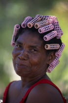 Head and shoulders portrait of Creole woman with her hair in pink plastic curlers.