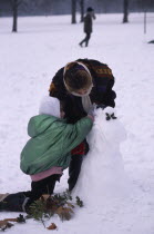Two girls building snowman decorated with holly leaves.cold  chill  2 European Great Britain Kids Londres Northern Europe UK United Kingdom British Isles