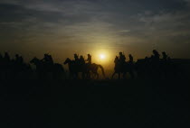 Hunting party on horseback silhouetted against sunset sky.