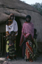 Afar women and children standing outside entrance of domed hut behind.home shelter nomadic culture African Eastern Africa Ethiopian Female Woman Girl Lady Kids Female Women Girl Lady