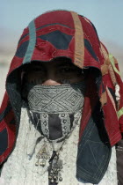 Head and shoulders portrait of Rasheida nomadic woman wearing embroidered and decorated head covering and veil revealing eyes and facial tattoo.Nomadic people originally from Saudi Arabia - now migra...