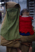 Muslim woman wearing full veil and carrying baby against her shoulder.Asia Asian Babies Bangladeshi Female Women Girl Lady Islam Kids Moslem Religion Religious Muslims Islam Islamic Female Woman Girl...