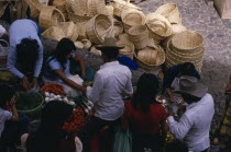 Looking down on customers at fruit and vegetable stall in market with woven baskets piled behind.American Hispanic Latin America Latino Mexican