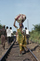 Young woman dressed in traditional local textiles carrying bundle on her head as she walks along railway track to market.African Central Africa Classic Classical Cloth Female Women Girl Lady Historic...