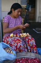 Woman in floral patterned skirt threading flower heads into garland at Juchitan street market.American Female Women Girl Lady Hispanic Latin America Latino Mexican One individual Solo Lone Solitary 1...