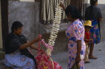 Woman vendor and customer at flower market stall looking at frangipani flower garlands.American Female Women Girl Lady Hispanic Kids Latin America Latino Mexican Female Woman Girl Lady