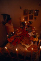 Woman lighting candles around altar for Day of the Dead covered with food and flowers.American Female Women Girl Lady Hispanic Latin America Latino Mexican One individual Solo Lone Solitary Religion...