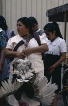 Woman holding turkey for sale at market standing amongst group of girls.