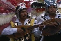 Musicians wearing elaborate feather head-dresses and costumes during Festival of Our Lady of GuadaloupeAmerican Hispanic Latin America Latino Mexican Religion Religious
