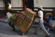 Traders using sack truck to transport wooden crates of fruit through street.American Hispanic Latin America Latino Lorry Mexican Van