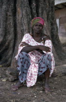 Portrait of woman seated at base of tree trunk wearing fabric of different printed patterns.African Boot Female Women Girl Lady One individual Solo Lone Solitary Senegalese 1 Female Woman Girl Lady S...