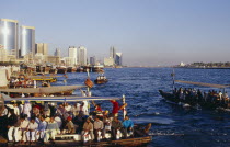 Abra water taxis with passengers on Creek with city skyline beyond. Dubayy United Arab Emirates Al-Imarat Al-Arabiyyah Al-Muttahidah Arabic Dubai Emiriti Middle East