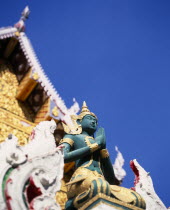Green and gold painted statue of Rama  an incarnation of Vishnu often depicted in temple statuary from the Ramakien National epic.  Point of decorated roof behind.Asian Prathet Thai Raja Anachakra Th...