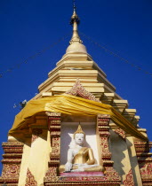 Seated Buddha statue in decorated recess below gold chedi wrapped in golden orange silk and hung with lights.Asian Prathet Thai Raja Anachakra Thai Religion Religious Siam Southeast Asia Siamese