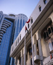 Two flag poles in front of contrasting styles of architecture  modern  mainly glass skyscraper behind facade of building in more traditional style.2 Classic Classical Dubayy Historical Older United A...