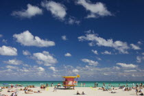 Crowded beach scene with pink lifeguard hut.