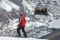 Skier on slopes with cable car ski lift overhead passing by.