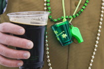 Detail of man wearing various green items whilst drinking pint of stout beer.